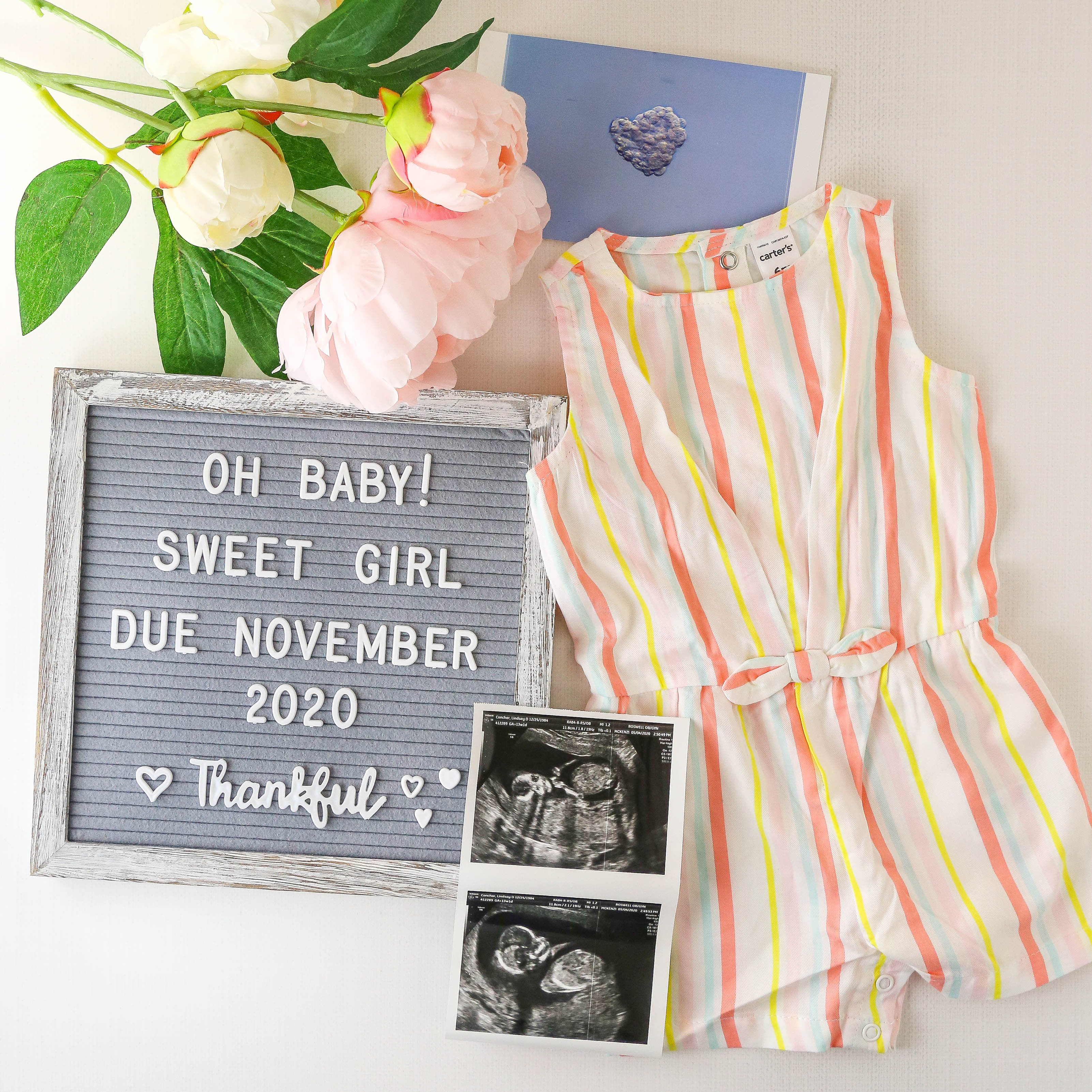 baby annoucement image with flowers, sonogram, baby outfit and letterboard